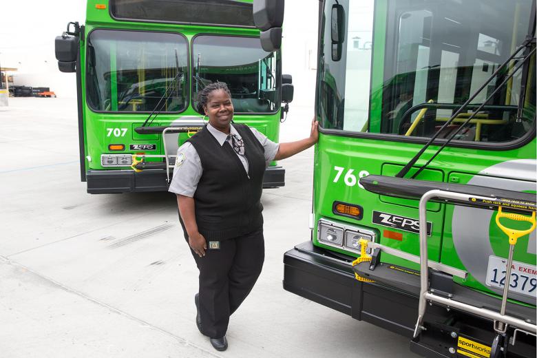 Female bus driver standing in front of two new fuel efficient busses 