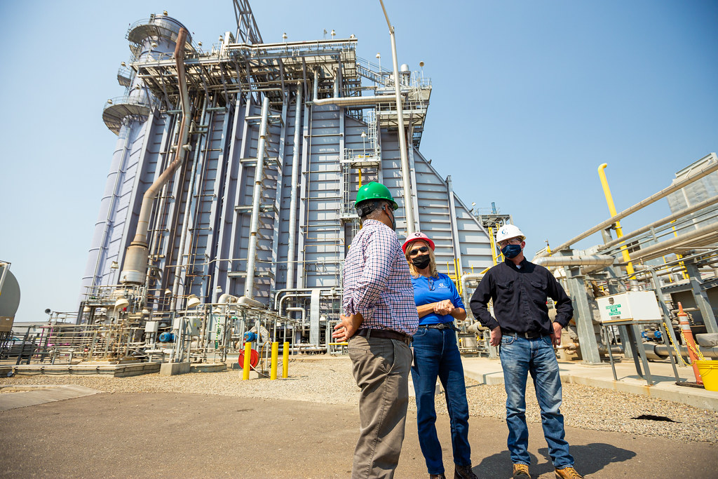 Image of facility with three people in front with hard hats having a conversation.
