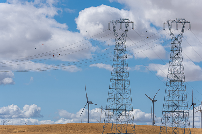 image of electrical towers with wind turbines behind it.
