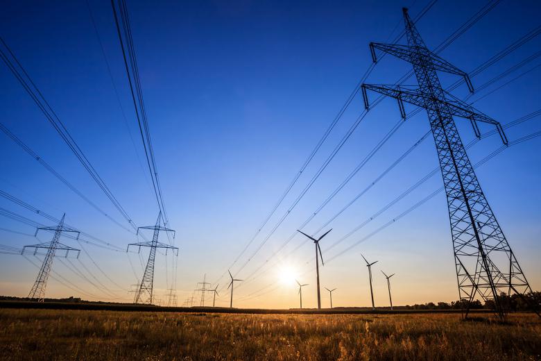 Sunrise image of desert fields with high voltage power lines stretching overhead with windmills in the distance