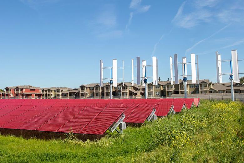 Image of solar panels with housing complexes in the background.