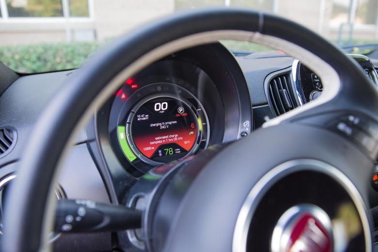 Image of an electric vehicle's interior. It shows a steering wheel and the dashboard where it displays a charing in progress status.