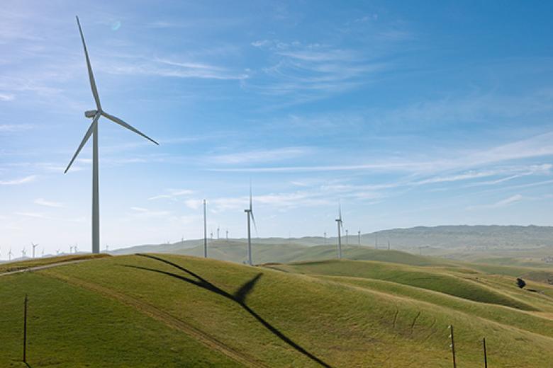 Wind turbines generate renewable energy on grassy hills under a clear blue sky.